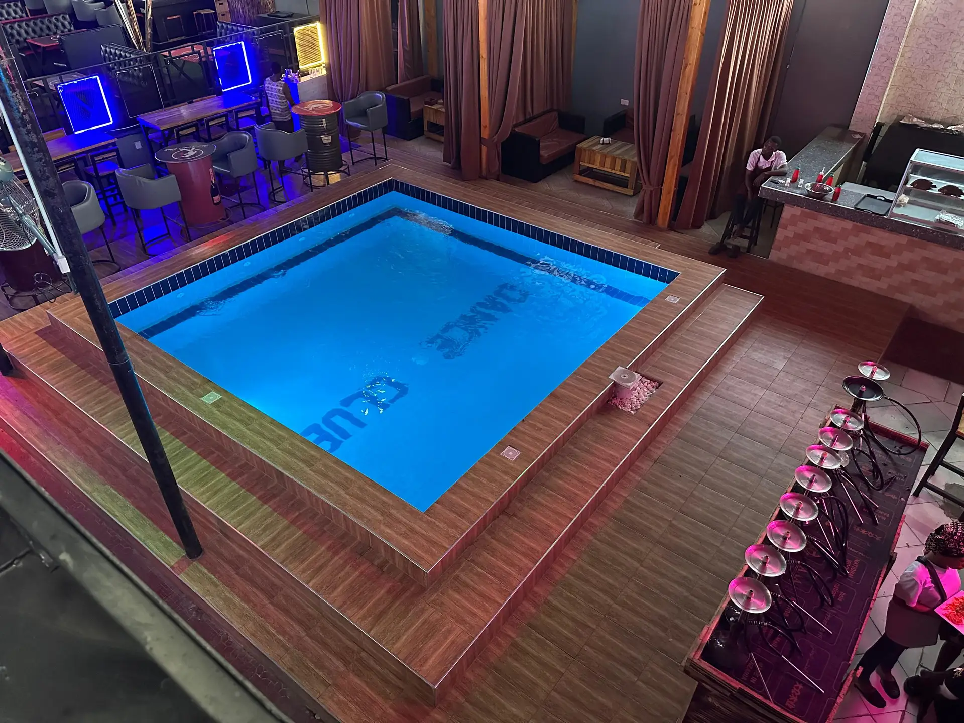 Club pool lit blue at night with a timber deck in Mwenge